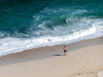 Aerial View of Man Walking on Sandy Beach Near Ocean Waves