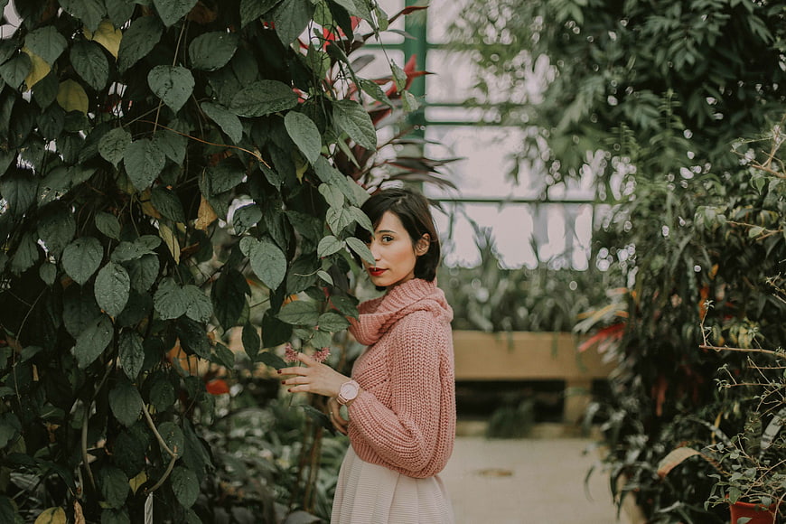 Woman in Pink Sweater Touching Leaves in Greenhouse