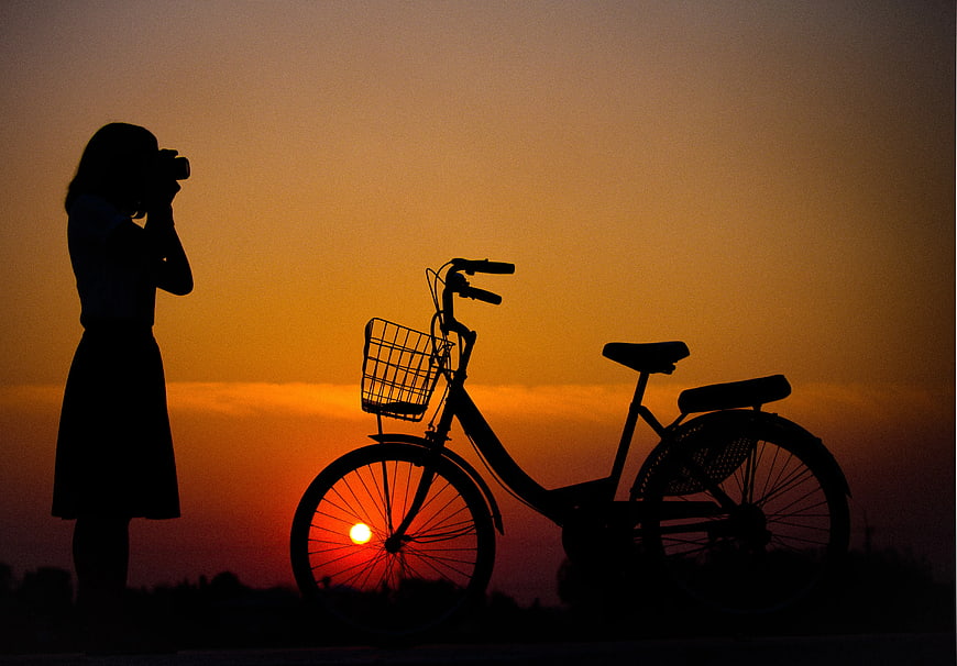 Silhouette of Woman Photographing Bicycle at Sunset