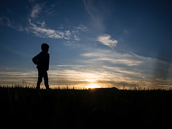 Silhouette of a child standing in a field at sunset
