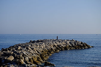 Lone Fisherman on Rocky Jetty in Calm Blue Sea