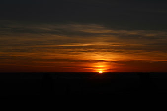 Silhouette of People Watching Orange Sunset Over Ocean Horizon