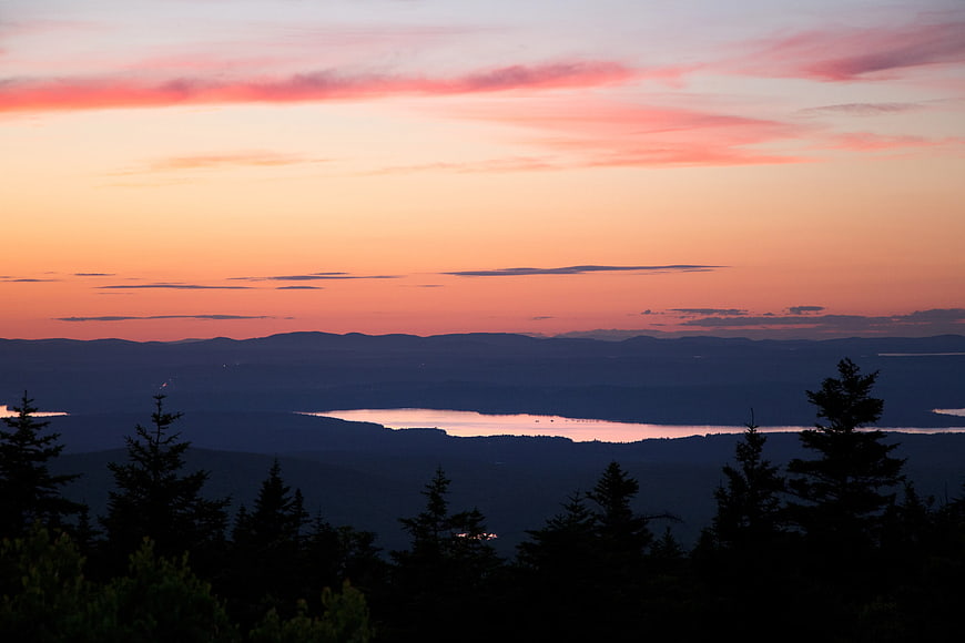 Sunset landscape with pine tree silhouettes and distant lake