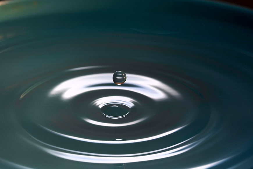 Macro shot of water droplet creating ripples in dark liquid
