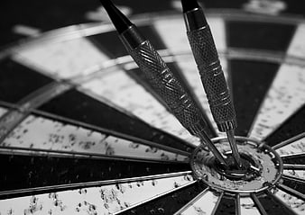Close-up of two darts hitting the bullseye on a worn dartboard
