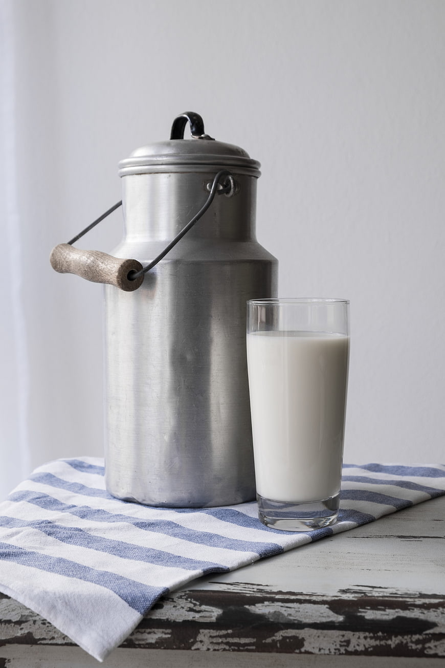 Vintage metal milk can and glass of milk on striped cloth