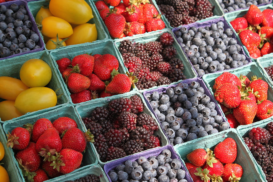 Colorful assortment of fresh berries and yellow tomatoes in market crates