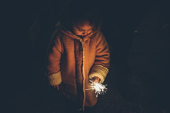Child holding sparkler at night in winter coat