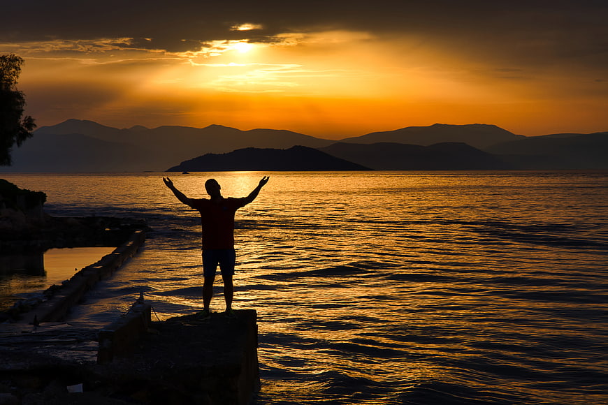 Silhouette of Man with Arms Raised at Sunset by the Sea