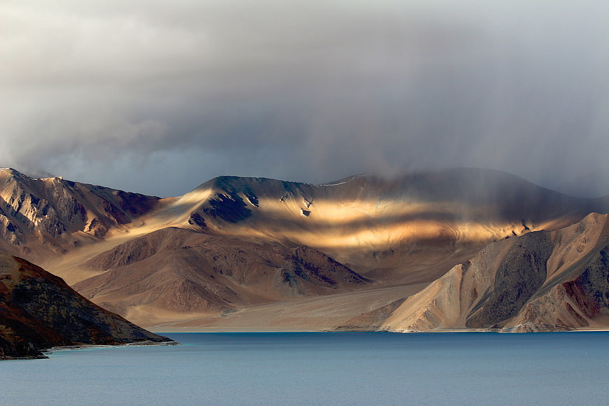 Dramatic sunlight illuminating arid mountains above a calm blue lake