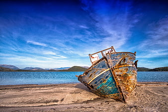 Rusty abandoned boat wreck on sandy beach with blue sky