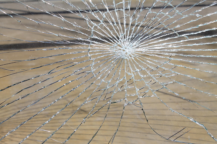 Close-up of shattered glass pane with radial cracks and splintered shards