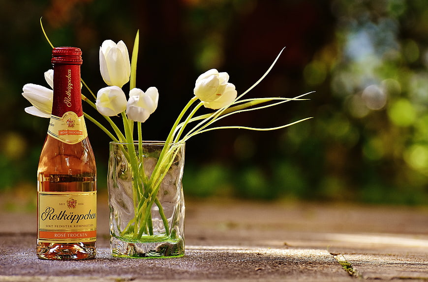 Rothkappchen Rosé Wine Bottle with White Tulips on Wooden Table