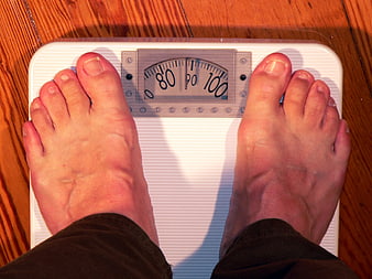 Bare feet standing on a bathroom scale with a mechanical dial