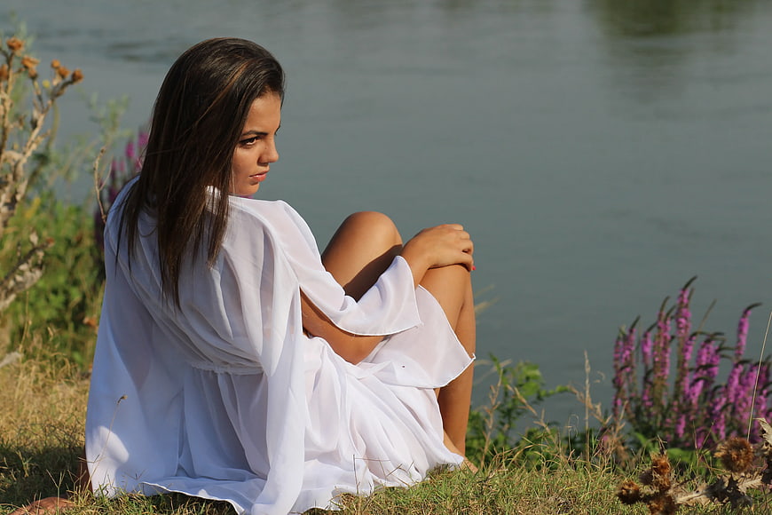 Pensive Woman in White Dress Sitting by Lake