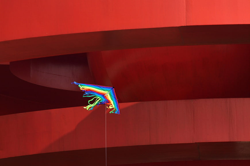 Rainbow kite flying against red architectural structure
