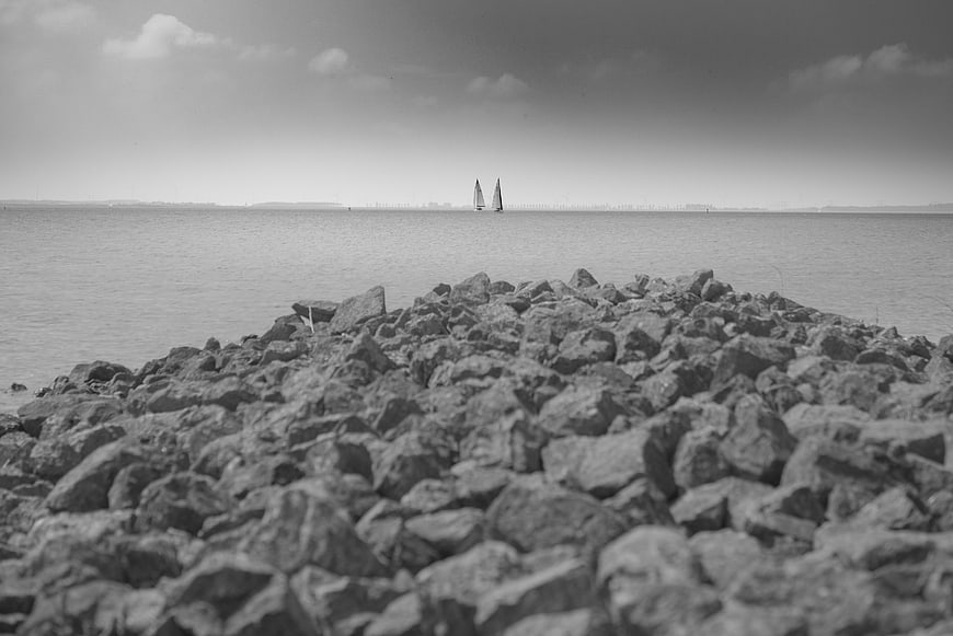 Black and white sailboats on calm sea with rocky foreground