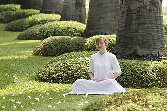 Woman meditating in white dress in a lush green garden