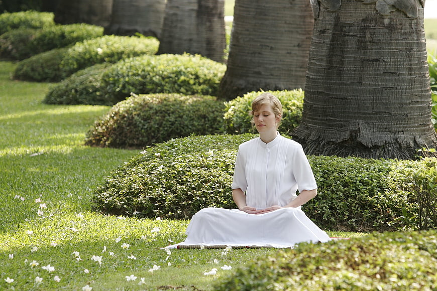 Woman meditating in white dress in a lush green garden