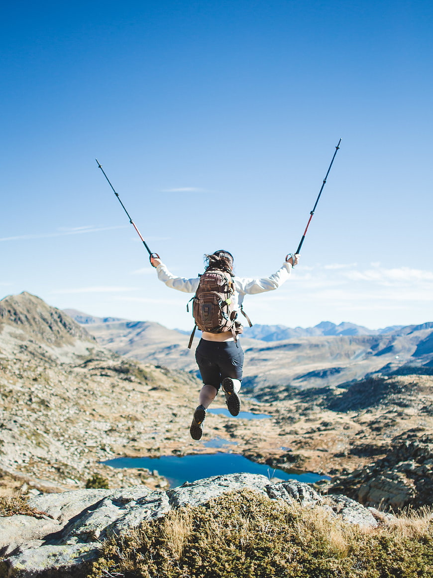Hiker jumping with trekking poles on mountain peak