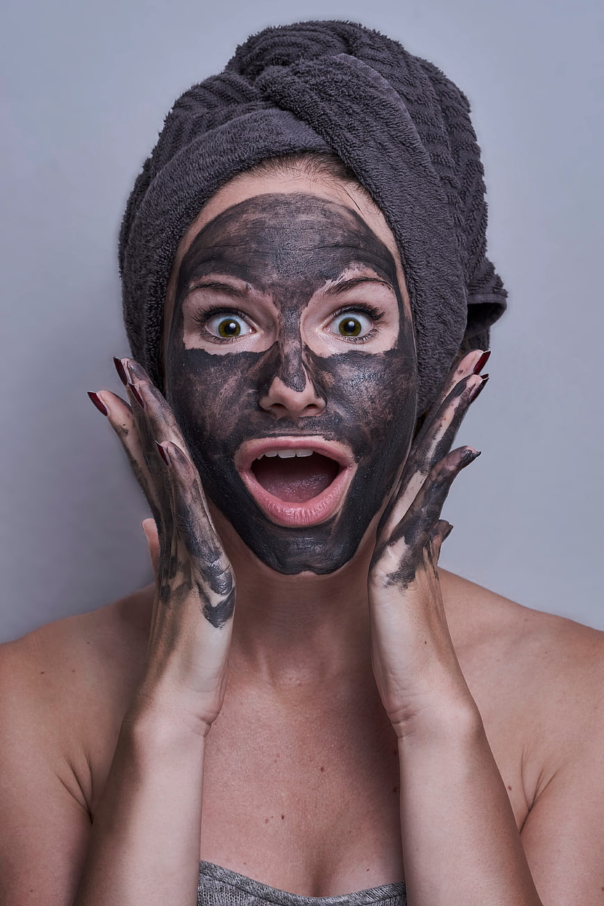 Woman with charcoal face mask and shocked expression