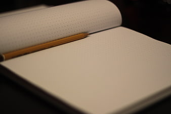 Open dotted notebook with yellow pencil on dark background