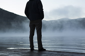 Man Standing on Wooden Dock Overlooking Misty Lake