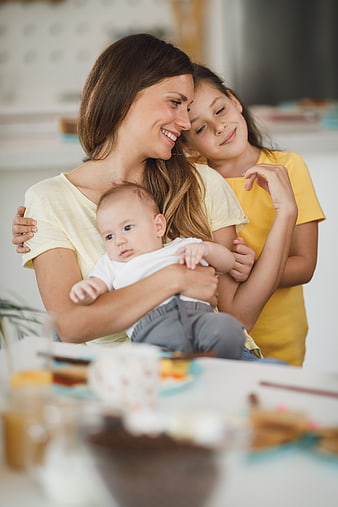 Happy mother hugging daughter and holding baby at home