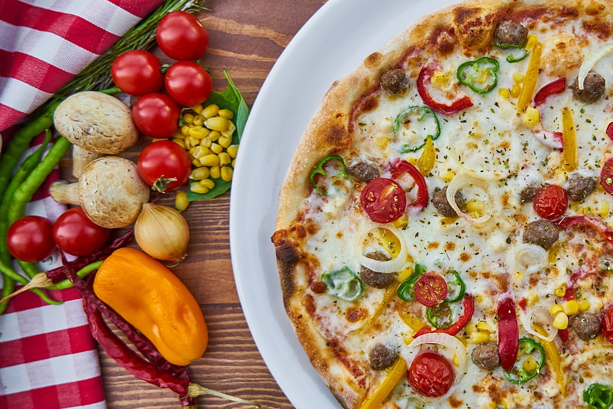Fresh vegetable pizza with raw ingredients on wooden table