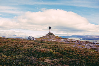 Lone Hiker Standing on Rocky Hilltop Overlooking Vast Moorland