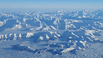 Aerial View of Snow-Covered Mountain Peaks Above Clouds