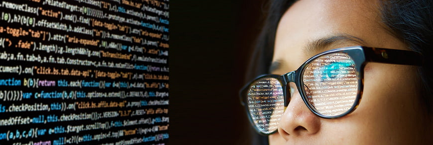 Close-up of woman programmer wearing glasses with code reflection