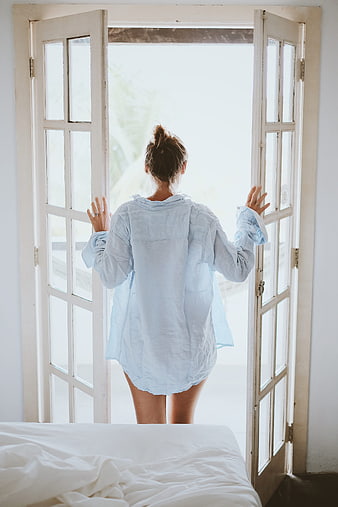 Woman in blue shirt opening white french doors to morning light