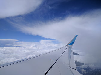 Airplane wing view above clouds and blue sky
