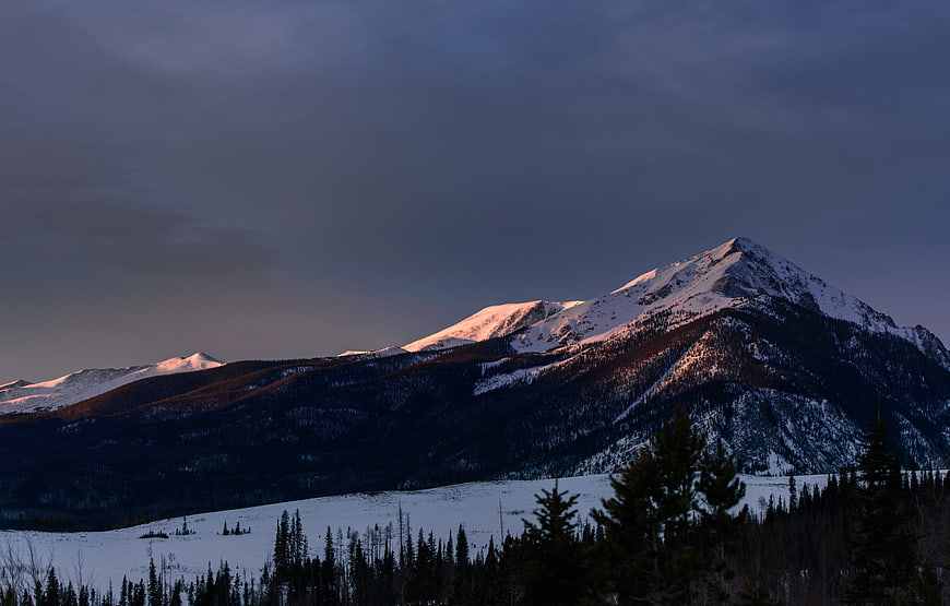 Snow-Capped Mountain Peak at Dusk with Foreground Forest