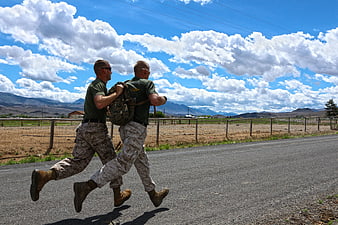 Two military men running with backpacks on a rural road