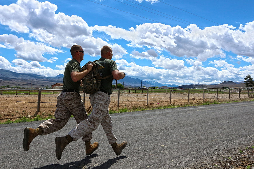 Two military men running with backpacks on a rural road