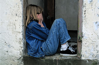 Sad girl sitting in doorway covering face with hands