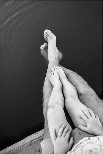Black and white photo of father and child legs by water