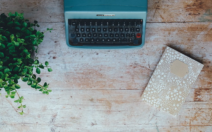 Vintage teal typewriter, notebook, and plant on rustic wood