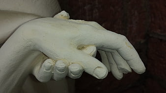 Close-up of white plaster statue hands against dark background