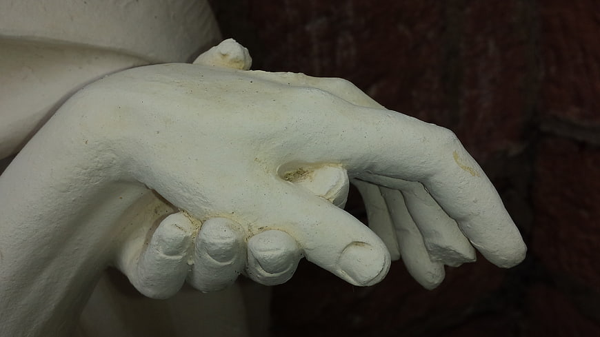 Close-up of white plaster statue hands against dark background