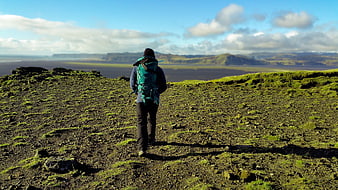Hiker with backpack overlooking vast mossy volcanic landscape