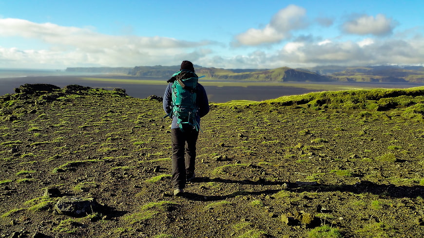 Hiker with backpack overlooking vast mossy volcanic landscape