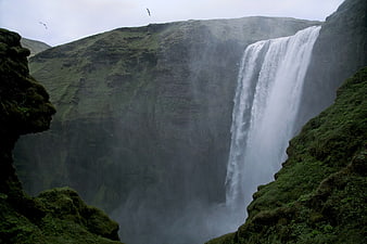 Majestic waterfall cascading down mossy green cliffs in misty landscape