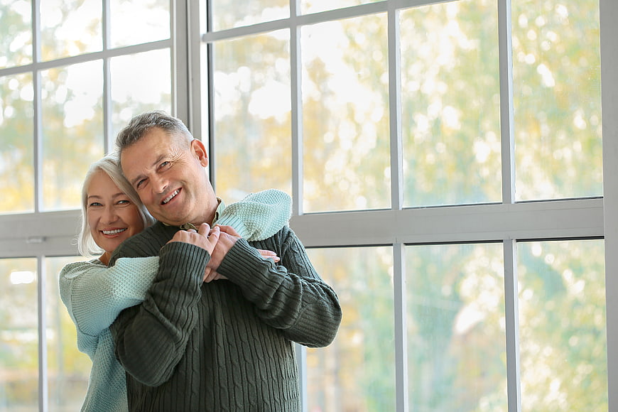 Happy Senior Couple Embracing by Window