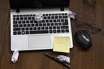 Laptop with crumpled paper and help sticky note on desk