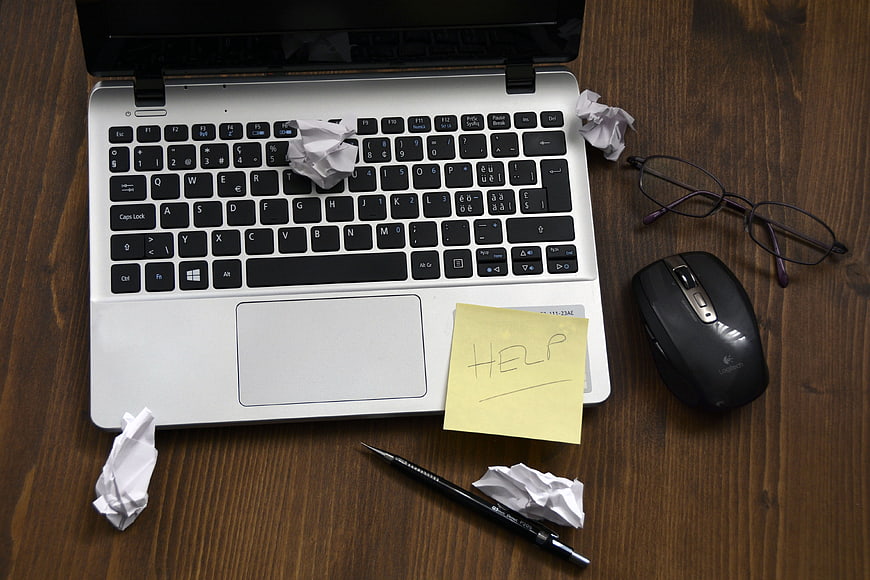 Laptop with crumpled paper and help sticky note on desk