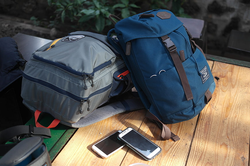 Two Travel Backpacks And Smartphones On Wooden Table