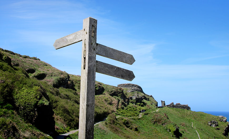 Weathered wooden trail signpost on a green coastal hillside